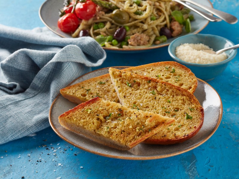 A plate of garlic bread with a dish of pasta in the background.